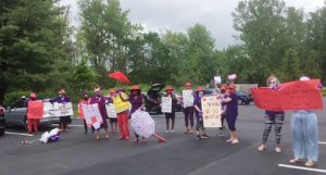 Members of five local Red Hat Society Chapters, representing Dutchess and Orange Counties, recite a group missive prior to Thursday’s meal delivery event, outside of the New Windsor Country Inn nursing home in New Windsor. Following the group gathering, participants held up their signs, chanting praises of appreciation to the essential workers, whom they supplied with a pizza lunch, beverages and snacks. The group held a similar in Poughkeepsie at Dutchess Assisted Living on Friday.