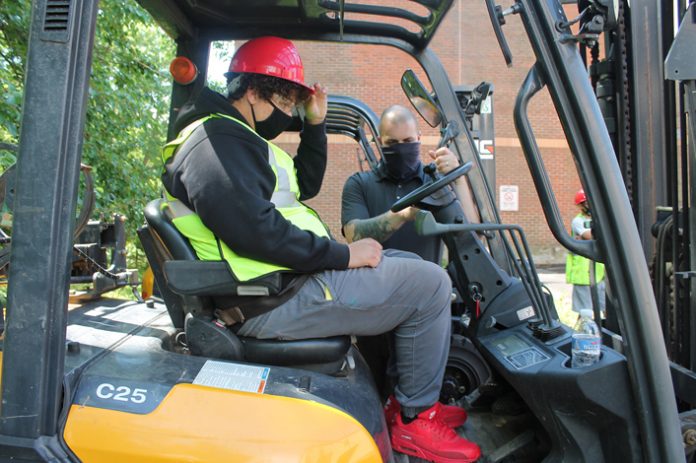 Ulster BOCES Motorcycle/Outdoor Power/Turf Management student Jordan Clarke (seated), from the Highland Central School District, practices operating a forklift under the guidance of Partner Rentals Logistics Manager Michael Pistone.