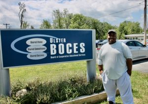 Henry Spencer, a 2020 Ellenville Central School District graduate who completed the CISCO & Cybersecurity program at the Ulster BOCES Career & Technical Center stands proudly in front of the Ulster BOCES sign. While Henry was a student, he served as a mentor for many struggling students, and he has enjoyed many successes since then, including acceptance into a four-year bachelor’s program at Mount Saint Mary College.