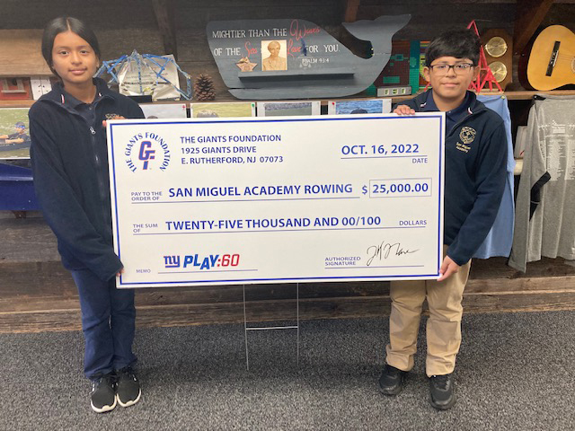 San Miguel Academy Rowing Team members: Isabella Luna and Ricardo Gunera hold up the check that was presented to their schools rowing program by the New York Giants on Sunday, October 16, 2022, at MetLife Stadium, where they and their teammates were invited out onto the field.