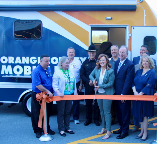 Orange County Clerk Kelly Eskew cuts the celebratory ribbon at the event to unveil the new Mobile DMV Unit. With Eskew (from left to right) are: Assemblyman Karl Brabenec, Deputy County Clerk-DMV Patricia McMullen, Orange County Sheriff Paul Arteta, District Attorney David Hoovler, Mark J.F. Schroeder, Commissioner of the New York State Department of Motor Vehicles, Orange County Legislator Rob Sassi (sunglasses on head) and Katie Bonelli, Chairwoman of the Legislature pose a photo.