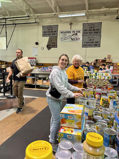 In front, Ava Marsich, Secretary of Loaves and Fishes and Irma Bahr-Madrid, President, assist with setting up the 25th Annual event, providing all the fixings for Thanksgiving meals to over 1000 families.