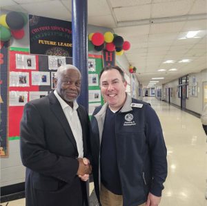Wesley Lee shakes hands with City of Poughkeepsie Planning and Development employee Bryan Cranna in front of Poughkeepsie High School’s Black History Month future leaders photo wall.
