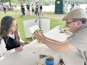 Sloop Club volunteer, Glenn Arnold, shows youngsters how to make a corn husk doll.